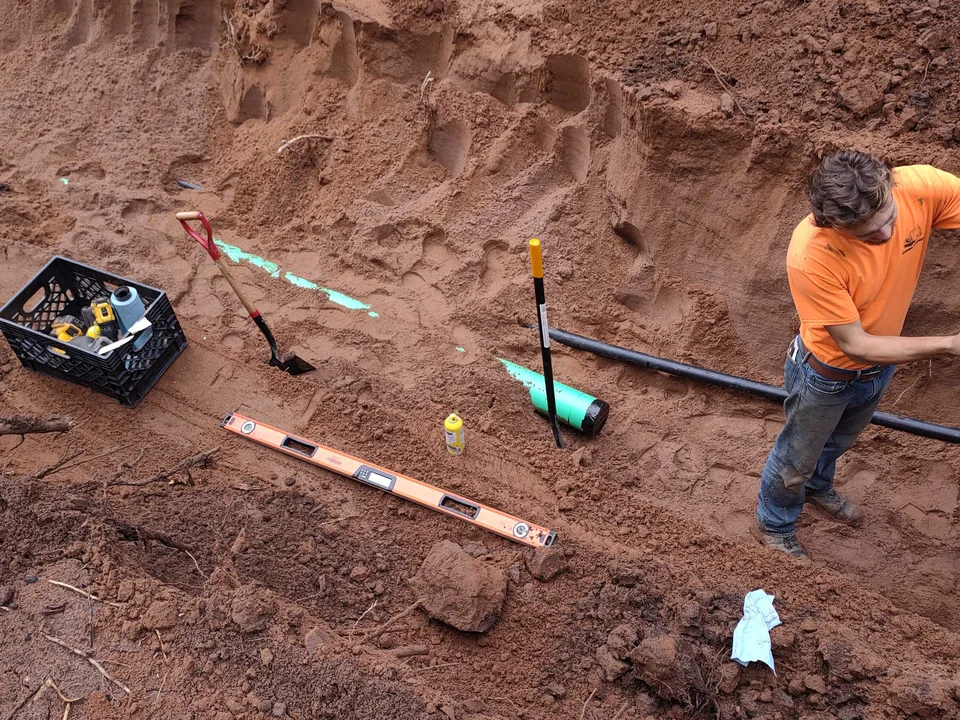 Crew member setting pipe to grade in an excavated trench