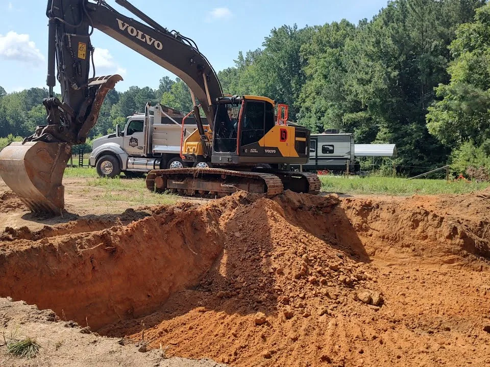 Excavator beside a freshly dug foundation hole with a dump truck behind, basement excavation