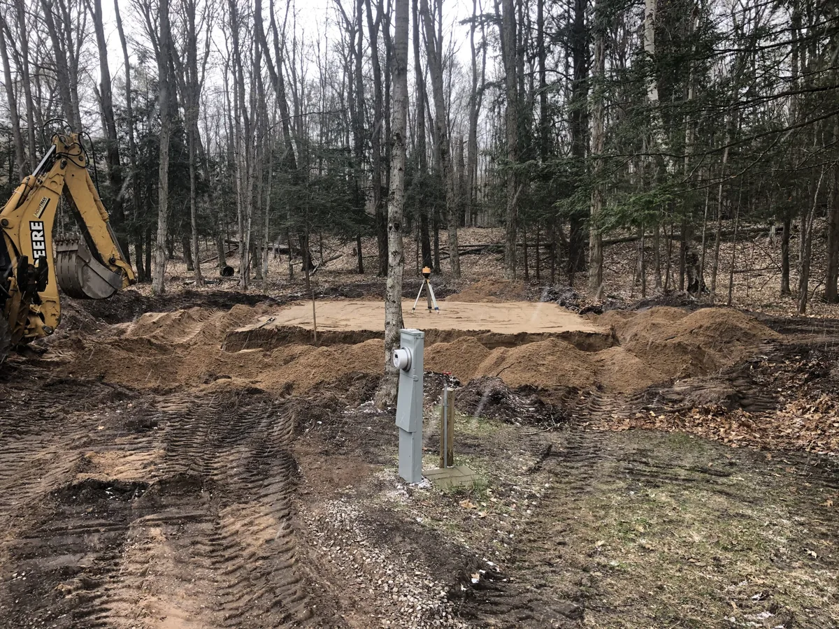 Backhoe and laser level at a foundation dig on a wooded lot, basement excavation