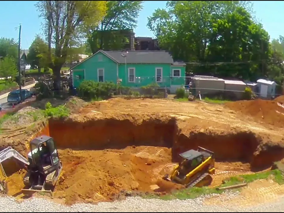 Wide view of a full basement hole on a residential lot with a dozer and skid steer, basement excavation