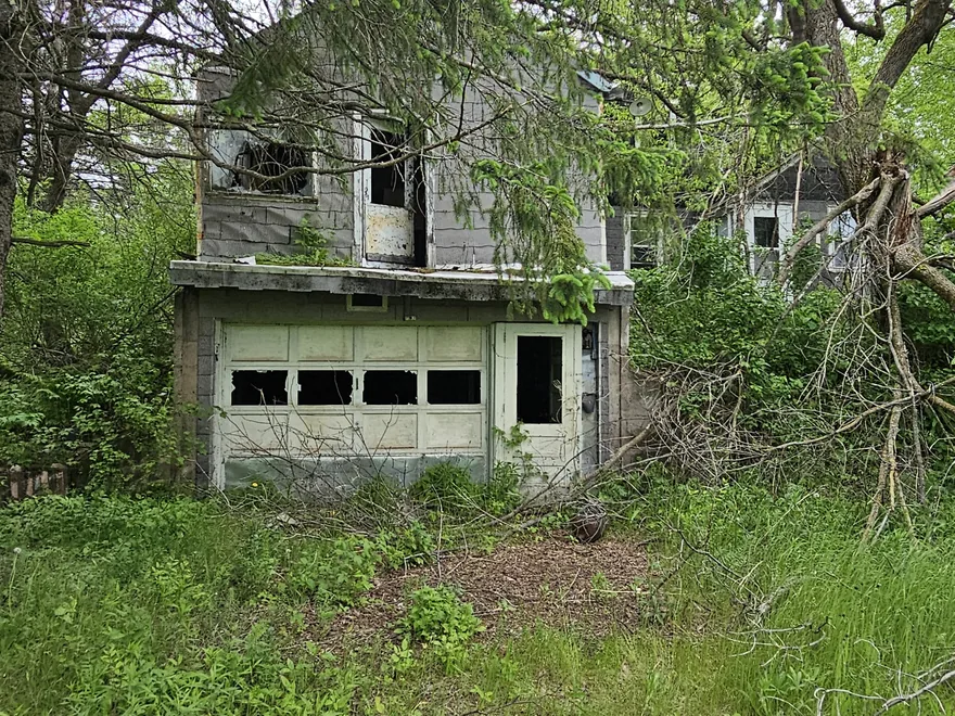 Weathered old house and garage in an overgrown yard, demolition