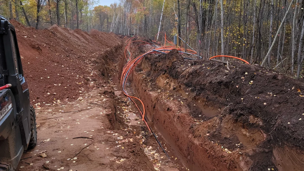 Utility trench with orange conduit dug along a road through fall woods