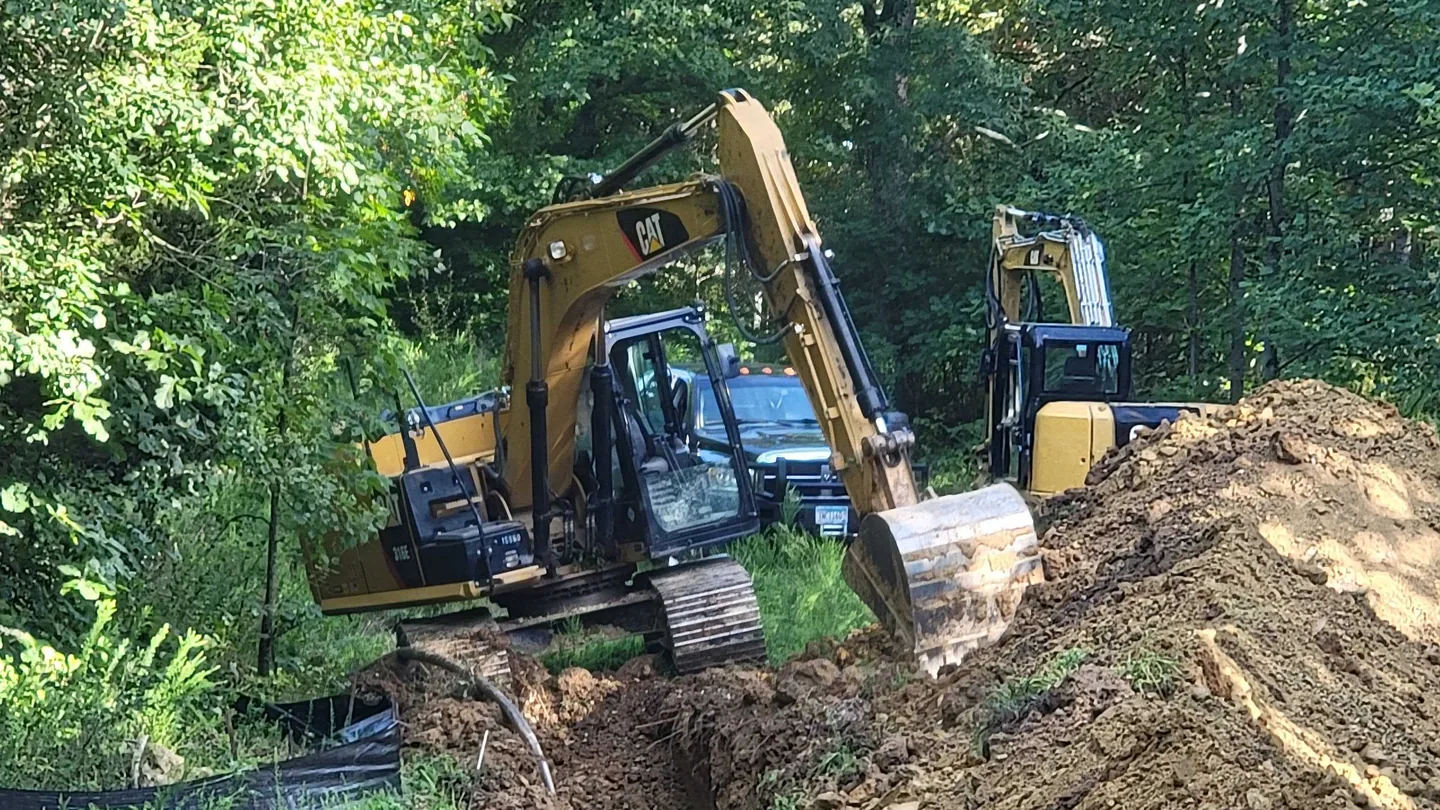 Excavation contractor digging a utility trench with an excavator on a wooded lot