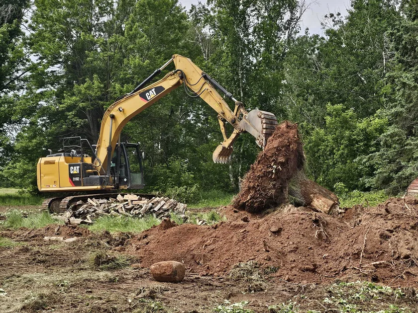 Excavator pulling a stump out of a grassy clearing, land clearing