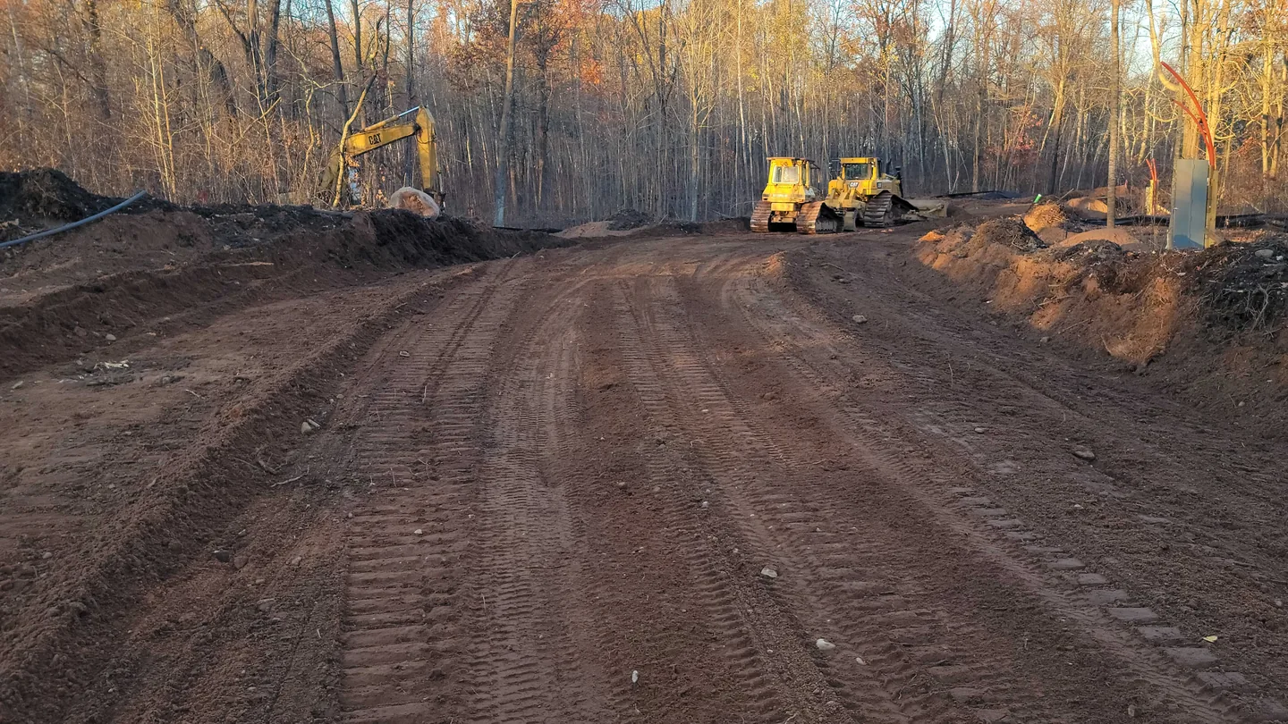 Long graded road through fall woods with machines working at the far end