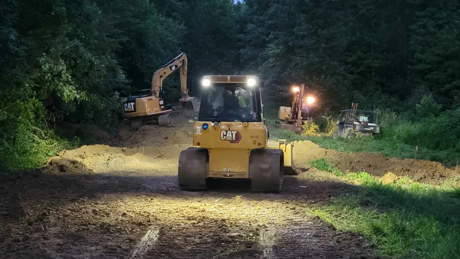 Bulldozer and excavator with work lights on a new road through the woods at dusk